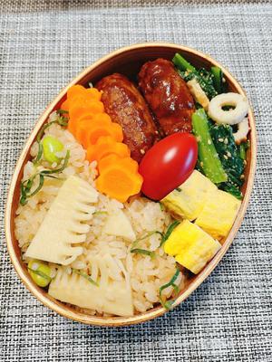 Pack the bento box. Start with rice, then add beef patties, rolled omelette, greens, carrots, and finally garnish with a cherry tomato. Done.