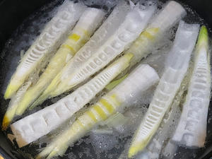 Peel and remove the old roots of the spring bamboo shoots, cut them in half, and blanch them in water.