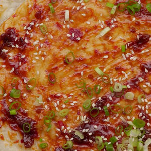 Brush sauce on the cooked pancake, sprinkle with sesame seeds and chopped scallions, and it's ready to enjoy.