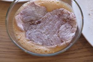 Take the pork cutlet, shake off excess flour, and dip it into the beaten egg. Coat both sides evenly, but do not soak it too long in the egg.