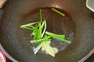 Heat oil in a pan and sauté the chopped scallions and ginger slices until fragrant.