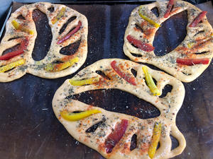 Once the dough has risen, top it with strips of red and yellow sweet peppers, brush with olive oil, and sprinkle with a little Italian mixed herbs, red pepper powder, and salt. Bake in the oven at 200 degrees Celsius for 15 minutes.