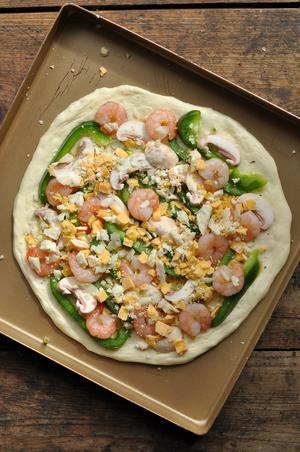 On the risen pizza dough, spread a layer of olive oil, sprinkle with herbs and salt, then add the sweet pepper, mushrooms, and shrimp, finishing with a sprinkle of cheese.