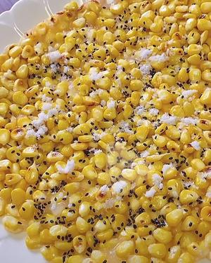 Fry corn kernels after blanching them in water until cooked! Remove and mix with milk, a pinch of salt, and a bit of starch. Heat oil in a pan, then press the corn mixture into a large cake, sprinkle with black sesame seeds, and when done, add some sugar for a sweet, crunchy, and delicious treat.