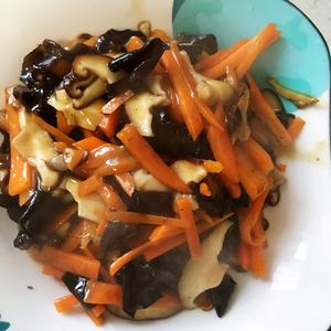 Start stir-frying. Once the oil is hot, add the ginger shreds. After a few seconds, add the carrot. Stir-fry for less than a minute, then add the wood ear mushrooms and shiitake mushrooms. The pan will be quite dry, so add a little water. Stir-fry for 2 minutes, ensuring the shiitake mushrooms are well cooked. Once the water is almost gone, add the prepared sauce, stir for a bit, then add salt. The pan will become increasingly sticky. Stir a few times and it's ready to serve.