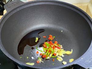 Then add the chopped scallions, red pepper, ginger slices, and minced garlic into the pan.